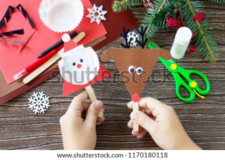 A child is holding Christmas Santa and Reindeer stics puppets. Handmade. Project of children's creativity, handicrafts, crafts for kids.
