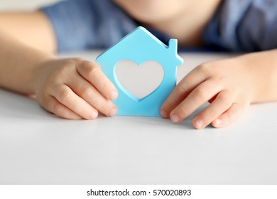 Child Holding Figure In Shape Of House, Closeup. Adoption Concept