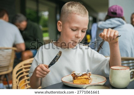 Child holding a fork and knife while eating a delicious pastry at a summer cafe table, enjoying a sweet snack during a family weekend trip