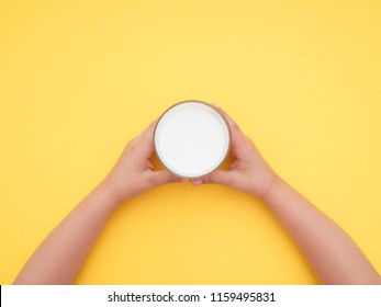 Child Holding A Glass Of Milk On Yellow Vibrant Background. Top View. Studio Shot.