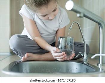 Child holding a glass under stream of clear transparent cold water from a tap. Close up shot of a young girl pouring a glass of fresh water from a kitchen faucet. Healthy Nutrition. World Water Day.