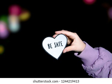 Child Holding Heart-shaped Pedestrian Safety Reflector With Text Be Safe Outdoors With Dark Background And Bokeh City Street Lights