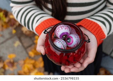 Child holding jar of halloween eyeballs amidst colorful autumn leaves - Powered by Shutterstock