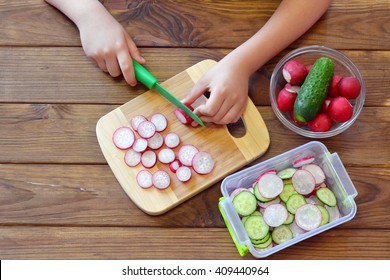 Child holding a kitchen knife and cut a radish. Child prepares a vegetable salad. Vegetables in a glass dish, a plastic container with sliced vegetables, a cutting Board on a wooden table  - Powered by Shutterstock