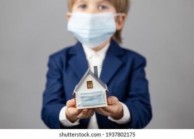 Child holding model house wearing protective medical mask in hands. Business during coronavirus COVID-19 pandemic concept