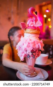 Child Holding Overshake In Cafe In Evening. Giant Dessert Of Milkshake, Donut, Marshmallow, Marmalade, Lollipop And Other Sweets.