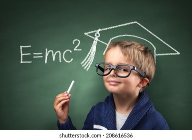 Child Holding Piece Of Chalk With E=mc2 And Mortar Board Drawing On Blackboard Concept For Genius Student, University Education And Future Aspirations