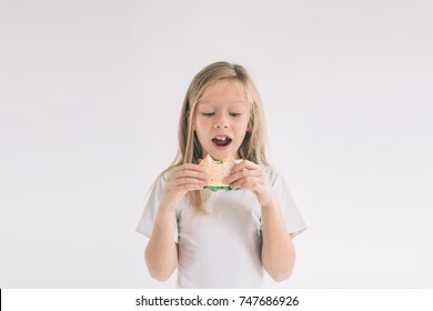 Child Holding A Piece Of Hamburger. Kid Eats Fast Food. Not Helpful Food. Very Hungry Baby. Girl Isolated On White Background