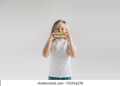 Child Holding A Piece Of Hamburger. Kid Eats Fast Food. Not Helpful Food. Very Hungry Baby. Girl Isolated On White Background