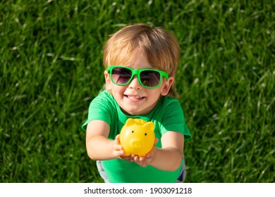 Child Holding Piggy Bank In Hands Against Green Spring Background. Fundraiser For Environmental Protection Concept