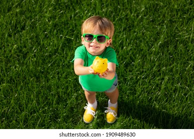 Child Holding Piggy Bank In Hands Against Green Spring Background. Fundraiser For Environmental Protection Concept