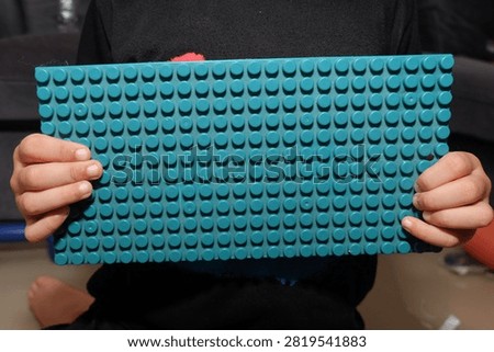 child holding a rectangular green plastic toy building baseplate horizontally in front of their chest.