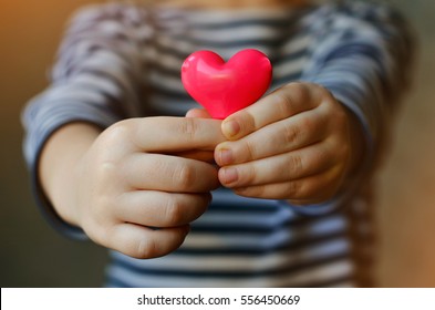 Child Holding A Small Pink Heart. Symbol Of Love, Family, Hope. Backgrounds For Cards On Valentine's Day. Backgrounds For Social Posters About The Preservation Of The Family And Children.