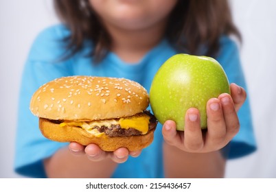 The Child Holds An Apple And A Burger In His Hands. Make Healthy And Unhealthy Food Choices