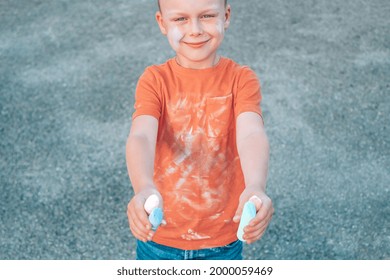 The Child Holds A Chalk In Both Hands On The Background Of Asphalt. Street Art, Kids Education. Chalk Stains On Clothes.Dirty Clothes. High Quality Photo