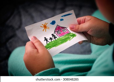 Child holds drawn house and family  Close up  Vignette 