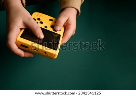 The child holds an electronic retro game console. Hand with electronic tetris game on green background.