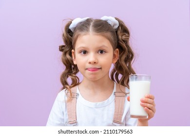 Child Holds A Glass Of Milk And Licks His Lips. Moustache From Milk Foam. A Little Girl Drinks Milk For Breakfast.