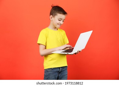 Child Holds A Laptop On An Orange Background. Boy 8-9 Years Old Uses A Computer On A Colored Background