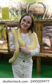 A child holds a large yellow python around their neck at a reptile exhibit, showcasing the interactive and educational nature of the display.