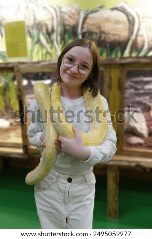 A child holds a large yellow python around their neck at a reptile exhibit, showcasing the interactive and educational nature of the display.