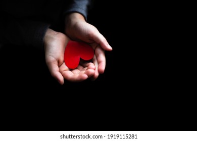 The child holds a red heart in his palms, hands close-up, black background, low key. Valentine's Day, Mother's Day, International Women's Day. Social project.