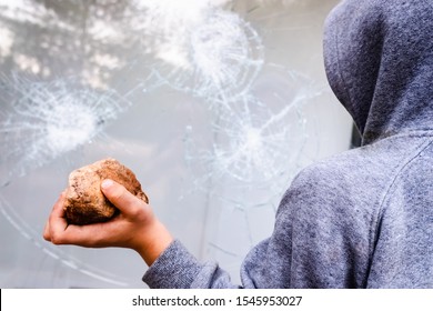 Child holds a stone to throw it against a glass and break a window.