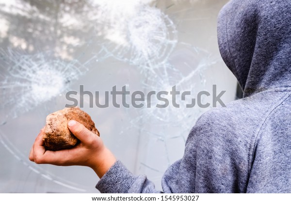Child holds a stone to throw it against a glass\
and break a window.