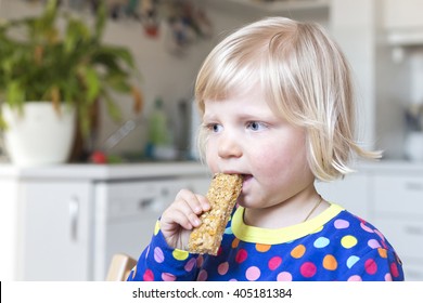 Child At Home Eating A Cereal Bar In Kitchen