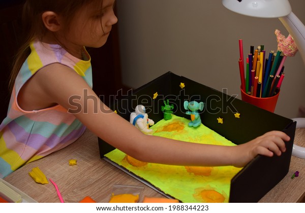 A\
child at home makes a space craft from light plasticine for school\
or kindergarten.  Little girl sculpts an astronaut, the surface of\
the moon and aliens. Little girl studying\
astronautics