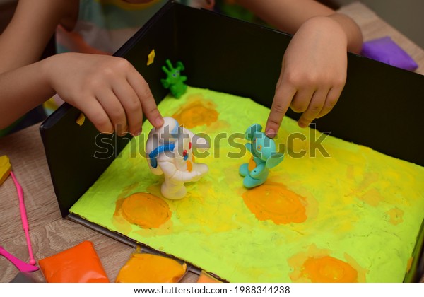 A\
child at home makes a space craft from light plasticine for school\
or kindergarten.  Little girl sculpts an astronaut, the surface of\
the moon and aliens. Little girl studying\
astronautics