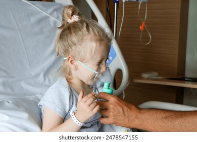 Child in hospital.Child is sick. A little girl breathes through an oxygen mask.The child is helped to hold the oxygen mask with his hands.Nebulizer. Photo of an oxygen mask on the face close.Health . - Powered by Shutterstock