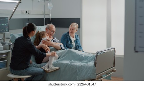 Child hugging sick grandpa in hospital ward bed at visit, comforting aged patient with illness. Kid and mother visiting senior man with IV drip bag and nasal oxygen tube. Visitors at clinic - Shutterstock ID 2126401547