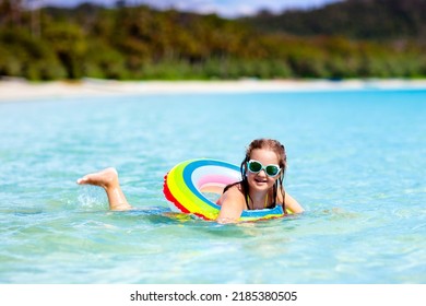Child With Inflatable Ring On Beautiful Beach. Little Girl Swimming In Exotic Sea. Ocean Vacation With Kid. Children Play On Summer Beach. Water Fun. Kids Swim. Family Holiday On Tropical Island.