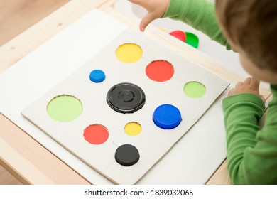 Child Inserting Different Size And Color Plastic Caps In Matching Holes.ergo Therapy Task For Education And Brain Exercise. DIY Play Game. Fine Motor Skills For Kids And Disabled