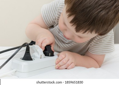 The Child Inserts A Plug Into An Electric Outlet, A Curious Boy Plays A Dangerous Game. The Idea Is Not To Leave Children Unattended.  The Probability Of Electric Shock.