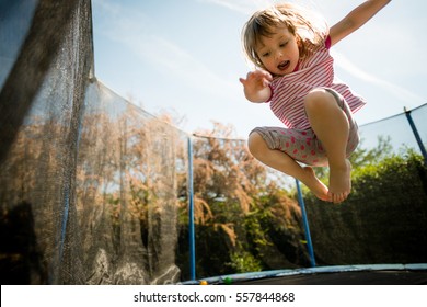 Child jumping high on big trampoline outside in garden