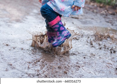 Child jumping in the muddy puddle; closeup of boots