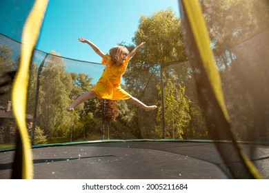 Child is jumping on trampoline with net for safety. Happy laughing kid outdoors in the yard on summer vacation. Jump high like a star 