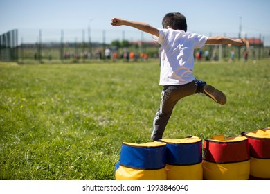 A Child Jumps Over An Inflatable Obstacle. Obstacle Course For Children. Pvzhkov Training For Schoolchildren. The Playful Boy Jumped Over A Cube Of Soft Material.