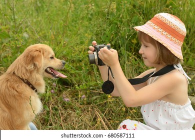 Child, Kid Photographer (a Little Girl) With A Camera Taking Pictures Of The Dog