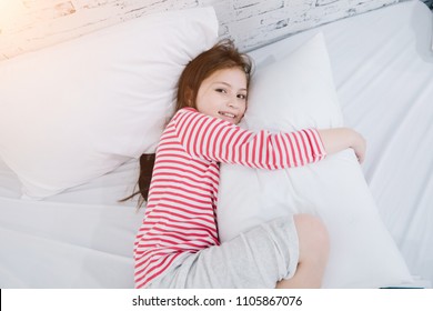 Child In Kindergarten,kid In Nursery School, Cute Girl Or Daughter Hugging The Pillow At Home In Bed Room.Children Concept.