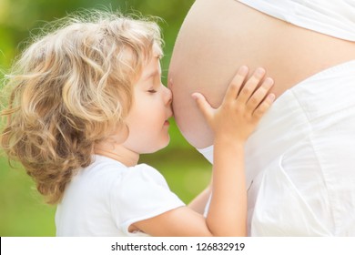 Child kissing belly of pregnant woman against spring green background