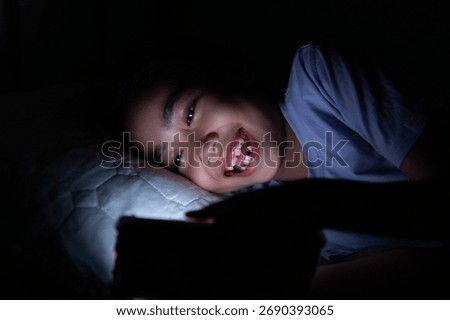 Child laughing while using smartphone at night. Screen time, late-night internet use concept.