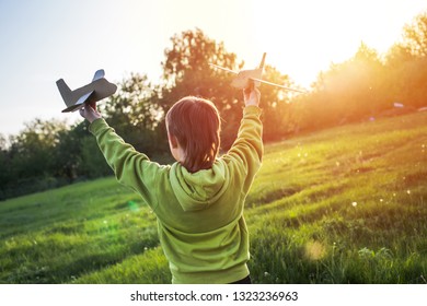 child launches paper airplane. boy in green jacket runs across field at sunset. Happy childhood. Walking on the street without a phone.