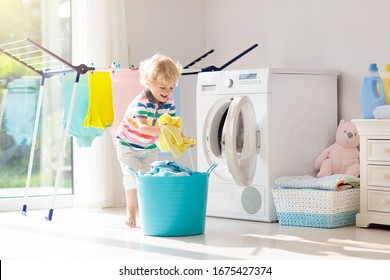 Child In Laundry Room With Washing Machine Or Tumble Dryer. Kid Helping With Family Chores. Modern Household Devices And Washing Detergent In White Sunny Home. Clean Washed Clothes On Drying Rack. 