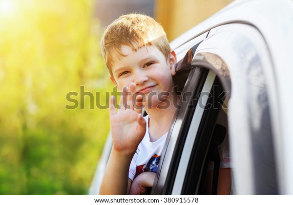 Child\
leaned out the window of a car and waving his\
hand.