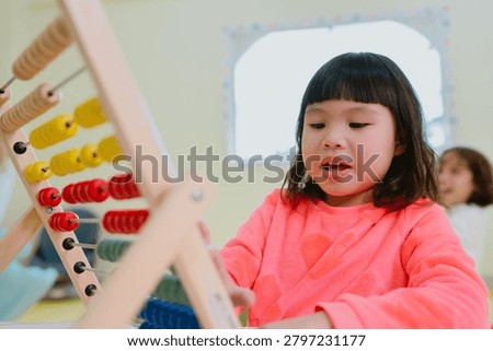 Child learning with abacus in classroom, focused girl solving math with colorful counting frame