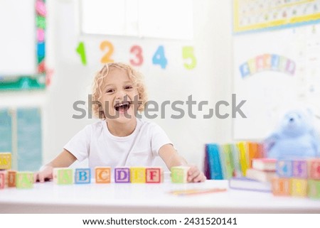 Child learning letters and numbers. Kid with colorful wooden abc blocks. Little boy spelling words with educational block toys. Kids doing school homework at white desk. Bedroom for preschool children