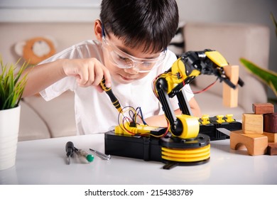 Child Learning Repairing Getting Lesson Control Robot Arm, Happy Asian Little Kid Boy Using Screwdriver To Fixes Screws Robotic Machine Arm In Home Workshop, Technology Future Science Education